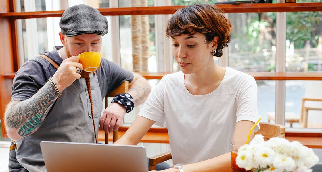 Young woman using laptop with man drinking coffee