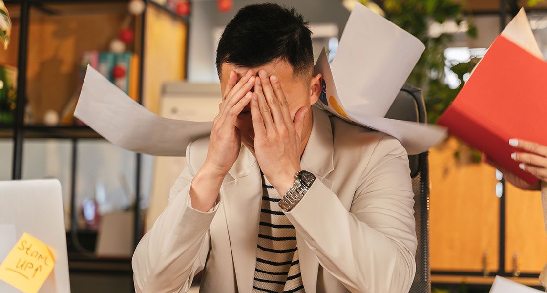 a man covering his face while sitting at a desk due to burnout and stress at work